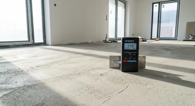 Glatter grauer Estrichboden in einem hellen, modernen Raum während der Trocknungsphase mit einem Feuchtigkeitsmessgerät.