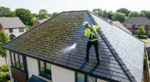 A professional roof cleaner using a pressure washer on a house roof with a clear before-and-after contrast.