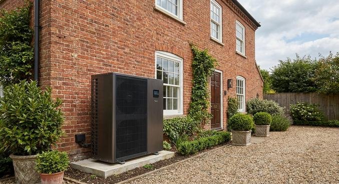A modern air-source heat pump unit installed outside a renovated traditional brick house in a green garden.