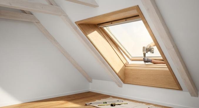Professional craftsman installing a new roof window in a bright, modern attic with sunlight.
